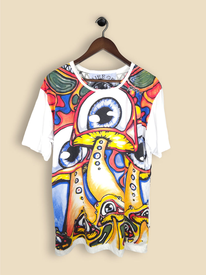 A white T-shirt with a vibrant, abstract design featuring colourful, large eyes and mushroom-like shapes in red, blue, yellow, and green.