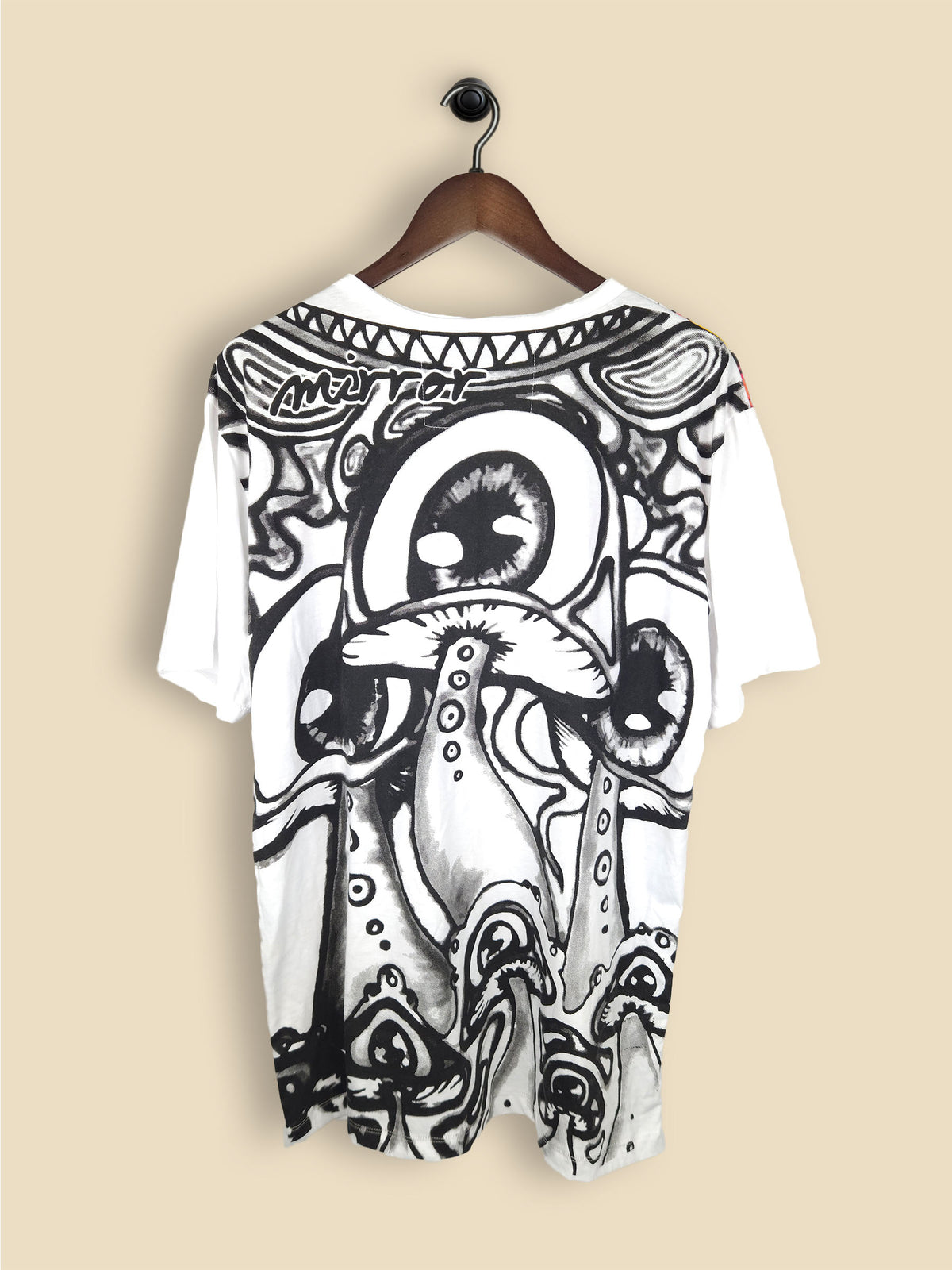 A white T-shirt with a vibrant, abstract design featuring colourful, large eyes and mushroom-like shapes in red, blue, yellow, and green.