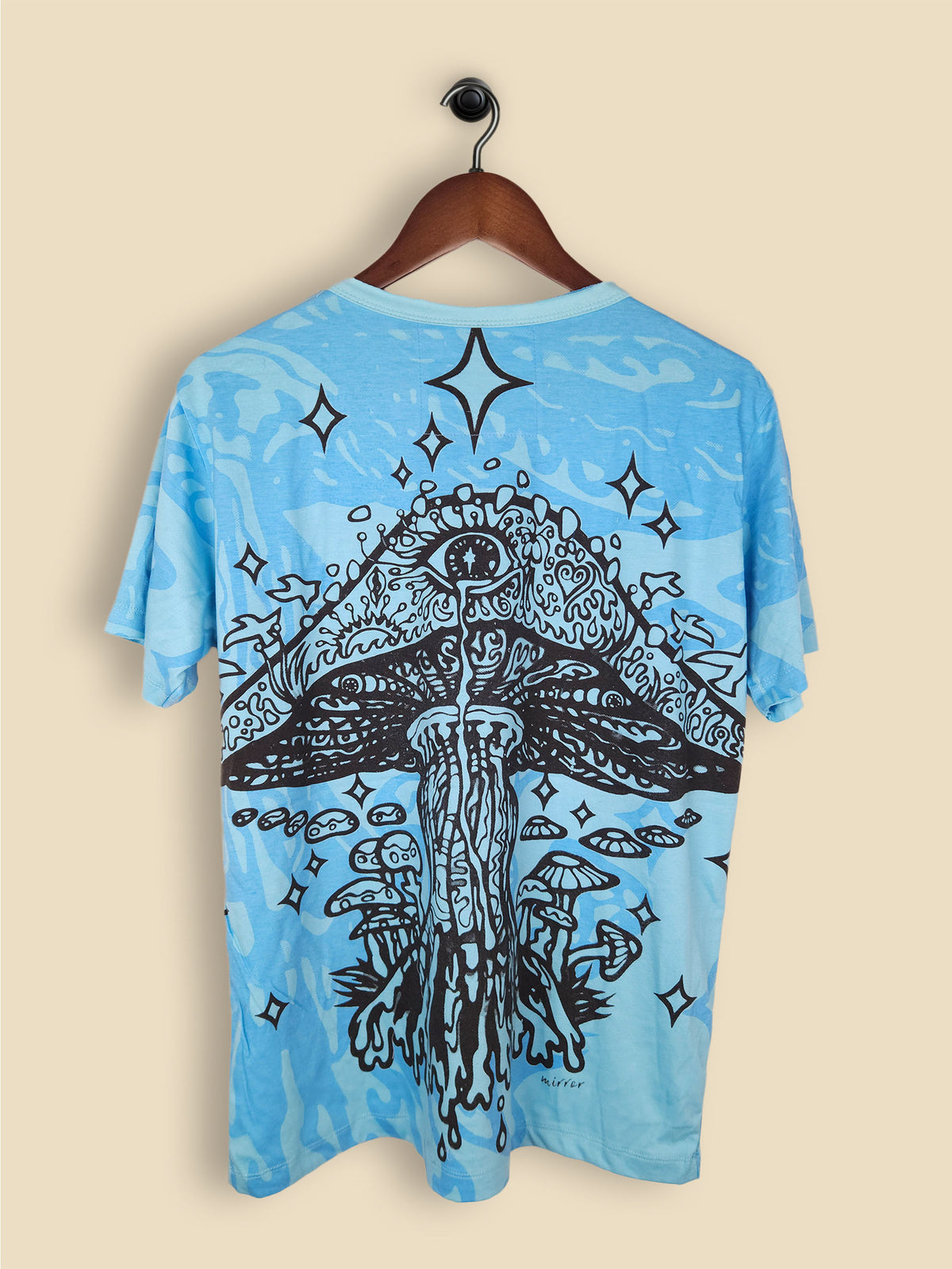 A blue T-shirt featuring a colourful, psychedelic mushroom design with smaller mushrooms, vibrant colors and star-like shapes.