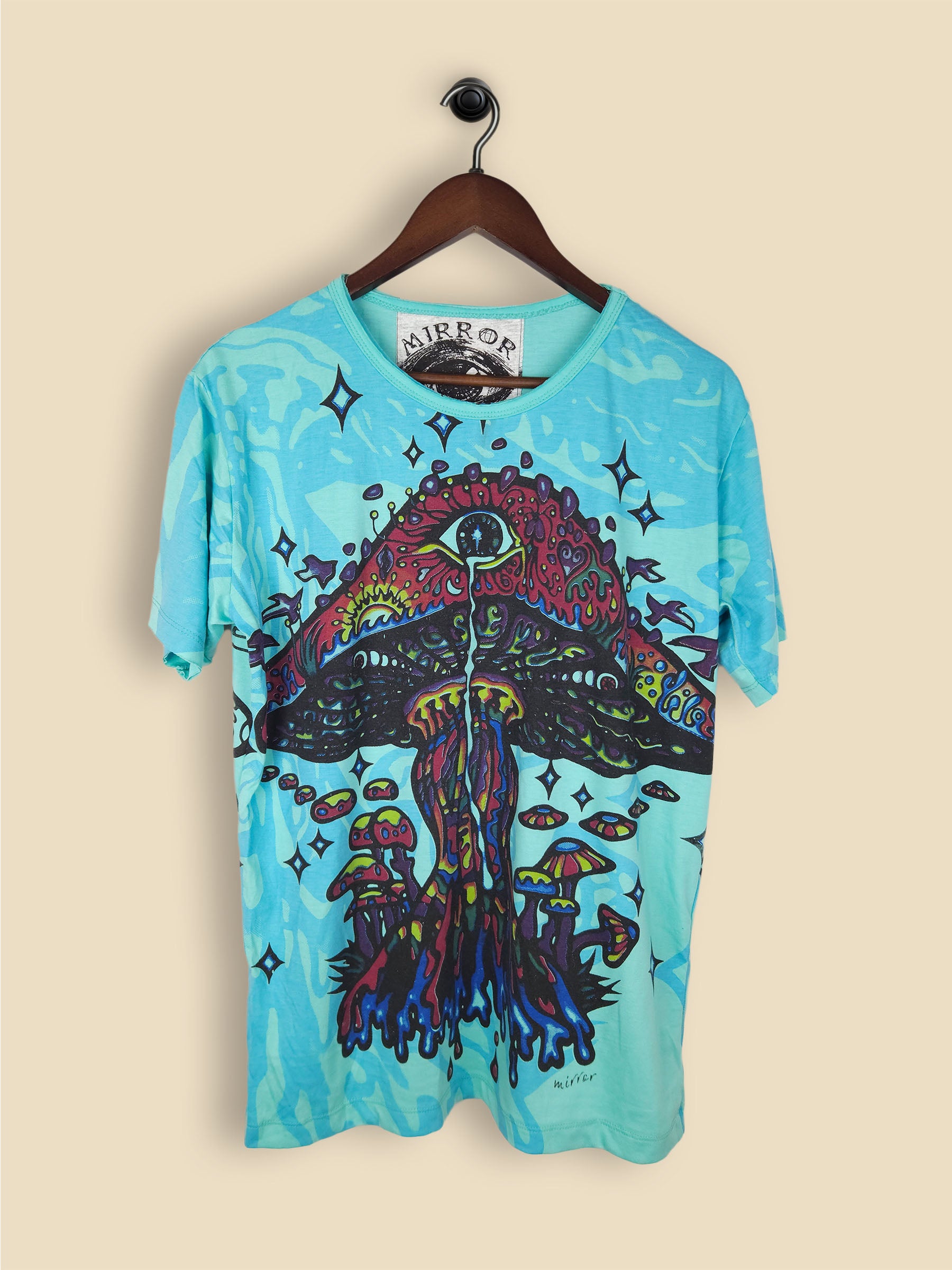 A turquoise T-shirt featuring a colourful, psychedelic mushroom design with smaller mushrooms, vibrant colours and star-like shapes.