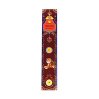 A rectangular incense package with a red background and colourful decorative elements. The package features a meditating figure at the top, a label in the centre that reads Cinnamon Happiness Incense,' and a tiger illustration near the bottom. The design includes floral patterns and a circular emblem.