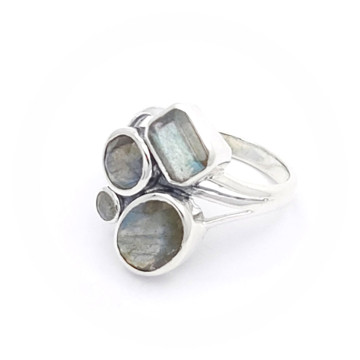 A silver ring featuring four labradorite stones of varying shapes and sizes. The stones include a rectangular, two circular, and an oval-shaped labradorite, all set in a modern, artistic design. The labradorite stones display a subtle play of colours, characteristic of the gemstone.