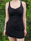 Person wearing a black sleeveless dress against a green leafy background