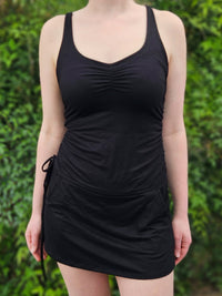 Person wearing a black sleeveless dress against a green leafy background