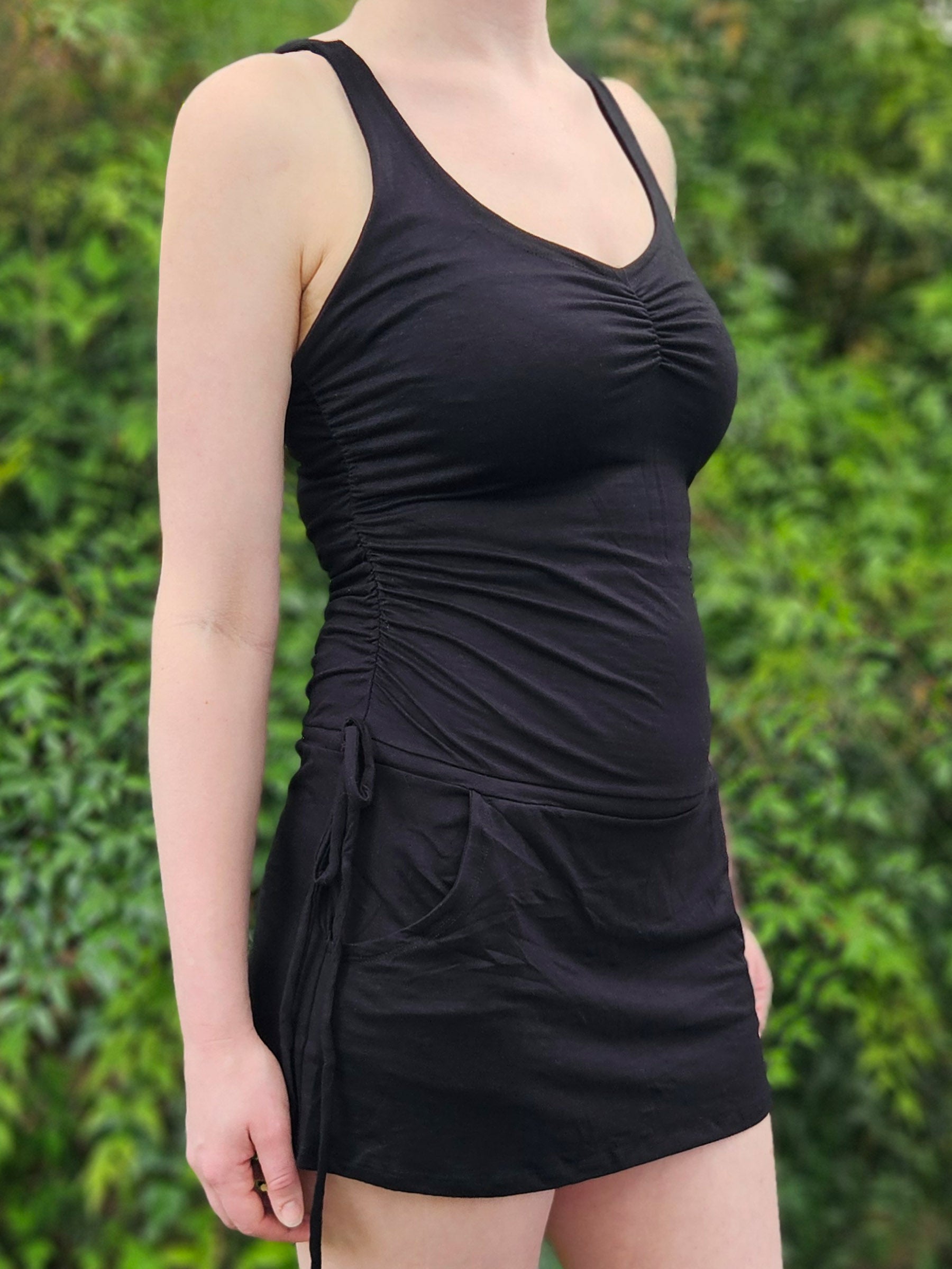 Person wearing a black mini dress against a green leafy background