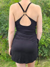 Person wearing a black mini dress with open back against a green outdoor background