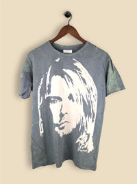 A slate green T-shirt featuring a bold, high-contrast stencil-style portrait of  Kurt Cobain with long hair in an off-white print. 