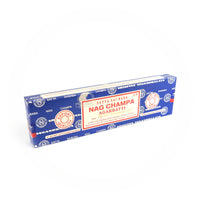 A rectangular blue box of Satya Sai Baba Nag Champa Agarbatti incense sticks is shown prominently. The box features a detailed red and white label with the text 'Satya Sai Baba Nag Champa Agarbatti,' 'Export Quality,' and 'Net Wt. 100g.' The packaging includes manufacturing details and certifications, highlighting its high quality and authenticity. This image captures the well-known and cherished design of the Satya Sai Baba Nag Champa incense, recognized for its distinctive fragrance and premium quality.