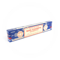 A rectangular blue box of Satya Sai Baba Nag Champa Agarbatti incense sticks is shown prominently. The box features a detailed red and white label with the text 'Satya Sai Baba Nag Champa Agarbatti,' 'Export Quality,' and 'Net Wt. 15g.' The packaging includes manufacturing details and certifications, highlighting its high quality and authenticity. This image captures the well-known and cherished design of the Satya Sai Baba Nag Champa incense, recognized for its distinctive fragrance and premium quality.