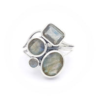 A silver ring featuring four labradorite stones of varying shapes and sizes. The stones include a rectangular, two circular, and an oval-shaped labradorite, all set in a modern, artistic design. The labradorite stones display a subtle play of colours, characteristic of the gemstone.