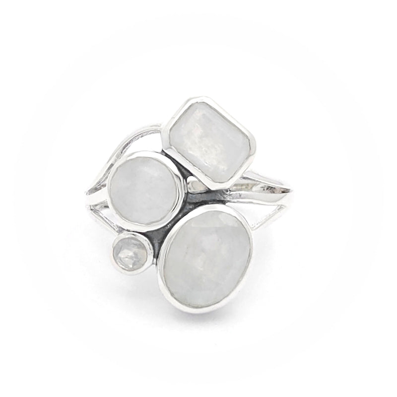 A silver ring featuring multiple moonstones in various shapes and sizes. The design includes a rectangular moonstone, two round moonstones, an oval moonstone, and a small circular moonstone, all set in an elegant silver band. The moonstones have a captivating, milky translucence, adding a touch of ethereal beauty to the ring.